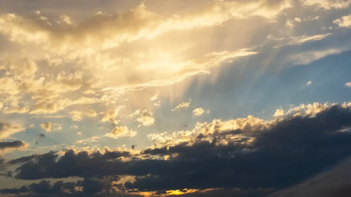 Sunset sky with golden clouds and sunbeams piercing through the clouds toward the horizon.