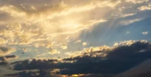 Sunset sky with golden clouds and sunbeams piercing through the clouds toward the horizon.
