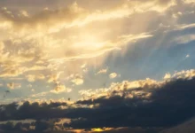 Sunset sky with golden clouds and sunbeams piercing through the clouds toward the horizon.