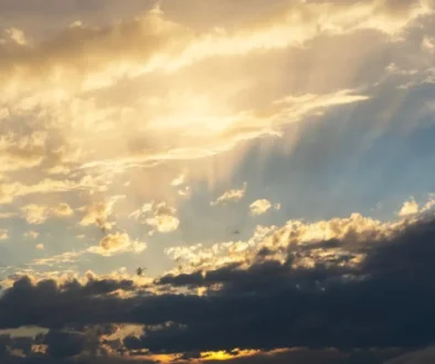 Sunset sky with golden clouds and sunbeams piercing through the clouds toward the horizon.