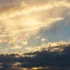 Sunset sky with golden clouds and sunbeams piercing through the clouds toward the horizon.