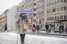 Stará žena jde s deštníkem po chodníku.
