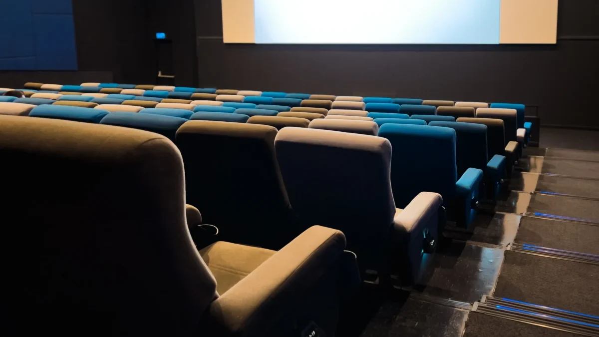 Empty cinema auditorium with blue and beige seats facing a large blank screen in a dark room.