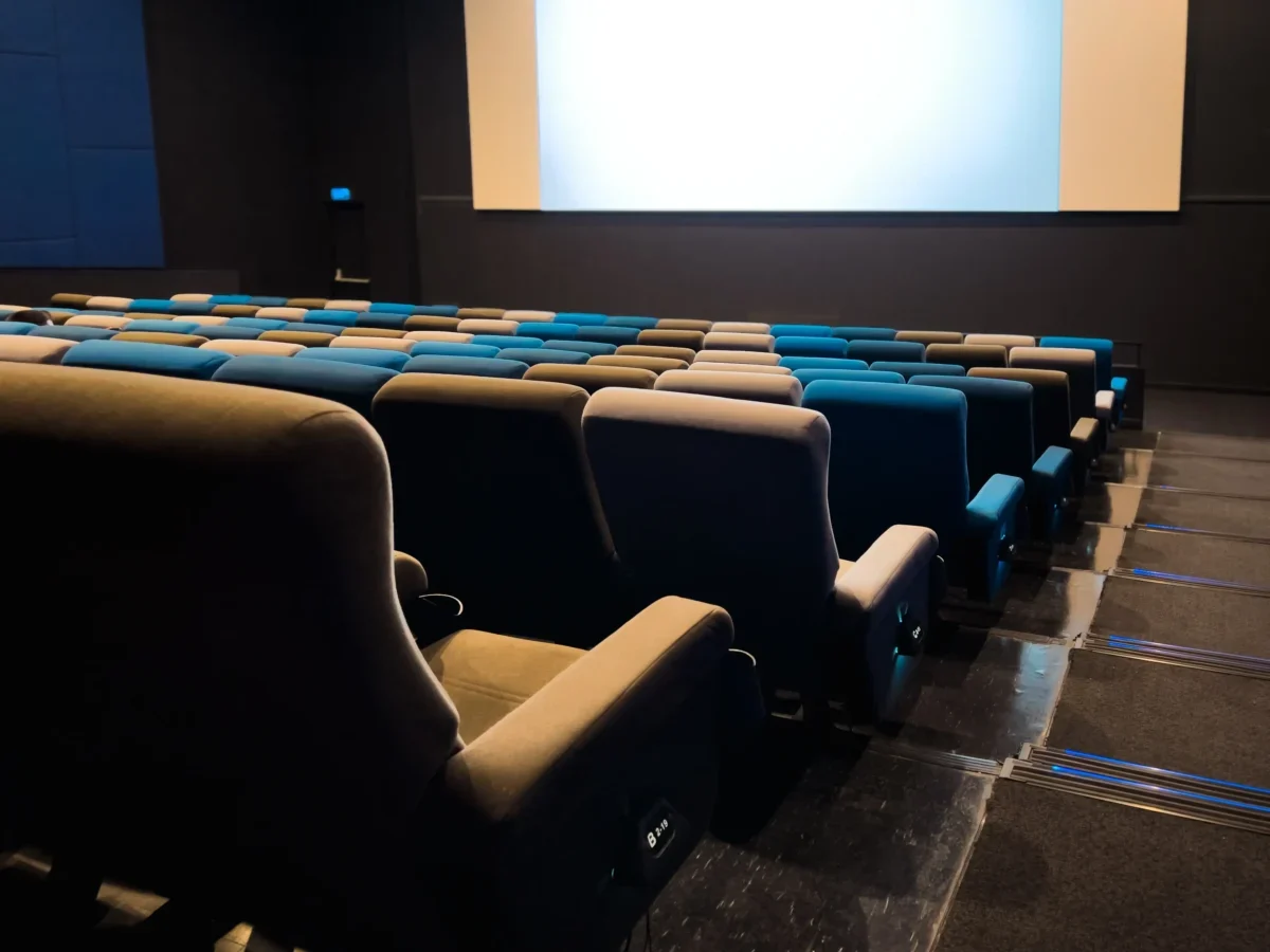 Empty cinema auditorium with blue and beige seats facing a large blank screen in a dark room.