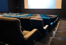 Empty cinema auditorium with blue and beige seats facing a large blank screen in a dark room.