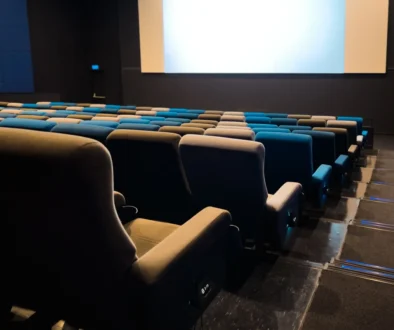 Empty cinema auditorium with blue and beige seats facing a large blank screen in a dark room.