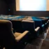 Empty cinema auditorium with blue and beige seats facing a large blank screen in a dark room.