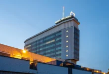 Tall glass-clad office tower with a lit Česká Televize sign on the rooftop, photographed at dusk against a blue sky.