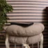 Beige cushioned stack with a black tablet resting on top, a leafy plant on the left, and a wooden-framed chair on the right against striped walls.
