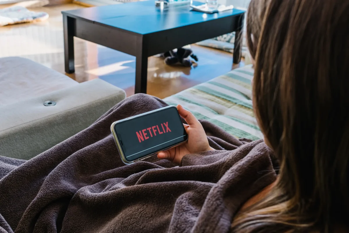 shutterstock_1828976036-2 | TVGURU.cz Žena je zachumlaná v dece a dívá se na mobilu na Netflix.