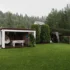 Rainy backyard scene with a white pergola, outdoor seating, and a green lawn under an overcast sky.