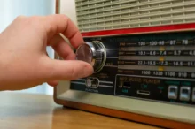 Close-up of a hand turning the chrome tuning knob on a vintage radio, with the FM/AM dial visible.
