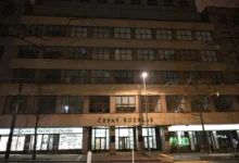 Nighttime view of a beige multi-story building with large windows and the sign 'Český Rozhlas' on the facade.
