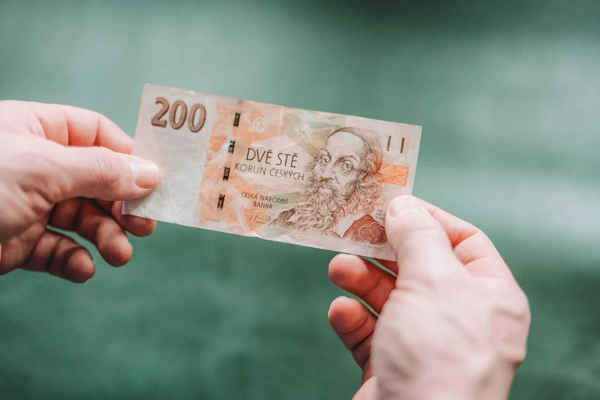 Je otázka koncesionářských poplatků tak důležitá | TVGURU.cz Člověk v ruce drží bankovku 200 Kč.