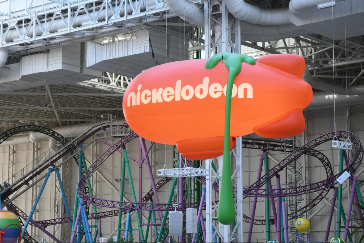 shutterstock_1912679608 1 | TVGURU.cz Large orange Nickelodeon balloon float inside an indoor amusement park with metal framework and colorful supports in the background, branding visible.