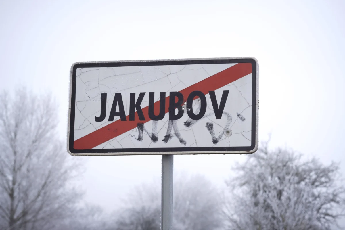 Snowy weathered road sign with a red diagonal stripe and graffiti covering the surface.