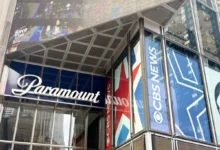Glass-fronted building with large blue banners reading 'Paramount' along the windows and a metal, paneled overhang above the entrance showing a colorful mural.