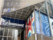 Glass-fronted building with large blue banners reading 'Paramount' along the windows and a metal, paneled overhang above the entrance showing a colorful mural.