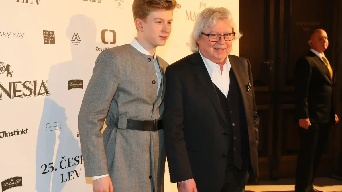 Two men posing on a red carpet at a film event, one in a gray suit with a belt and the other in a black suit, backdrop with sponsor logos.