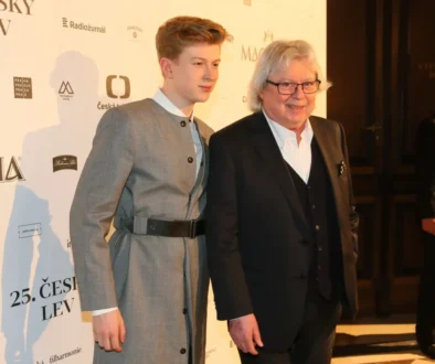 Two men posing on a red carpet at a film event, one in a gray suit with a belt and the other in a black suit, backdrop with sponsor logos.