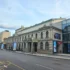 Historic beige building with arched windows and decorative cornices along a city street; modern glass building to the right; blue sky above.