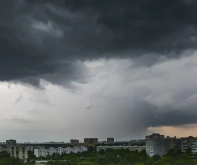 Dark storm clouds loom over a city skyline, with apartment blocks and trees below at dusk/light clouded horizon.