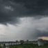 Dark storm clouds loom over a city skyline, with apartment blocks and trees below at dusk/light clouded horizon.