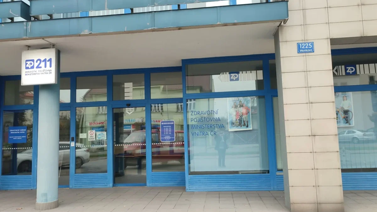 Blue-framed storefront of a Czech health insurance office (ZP 211) with glass doors and a street address plaque reading 1225 Wonkova on a beige tiled wall