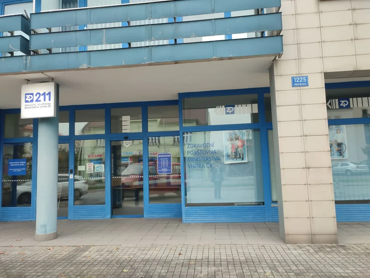 Blue-framed storefront of a Czech health insurance office (ZP 211) with glass doors and a street address plaque reading 1225 Wonkova on a beige tiled wall