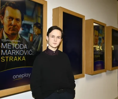 Mladý muž v černé bundě stojí u obrazu.