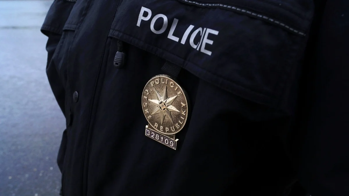 Close-up of a gold police badge with a star and a numbered plate hanging from a dark uniform that reads POLICE/REPUBLIC.