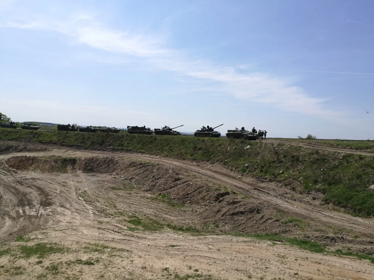 Line of military tanks parked along a dirt road at the edge of an embankment under a clear blue sky.