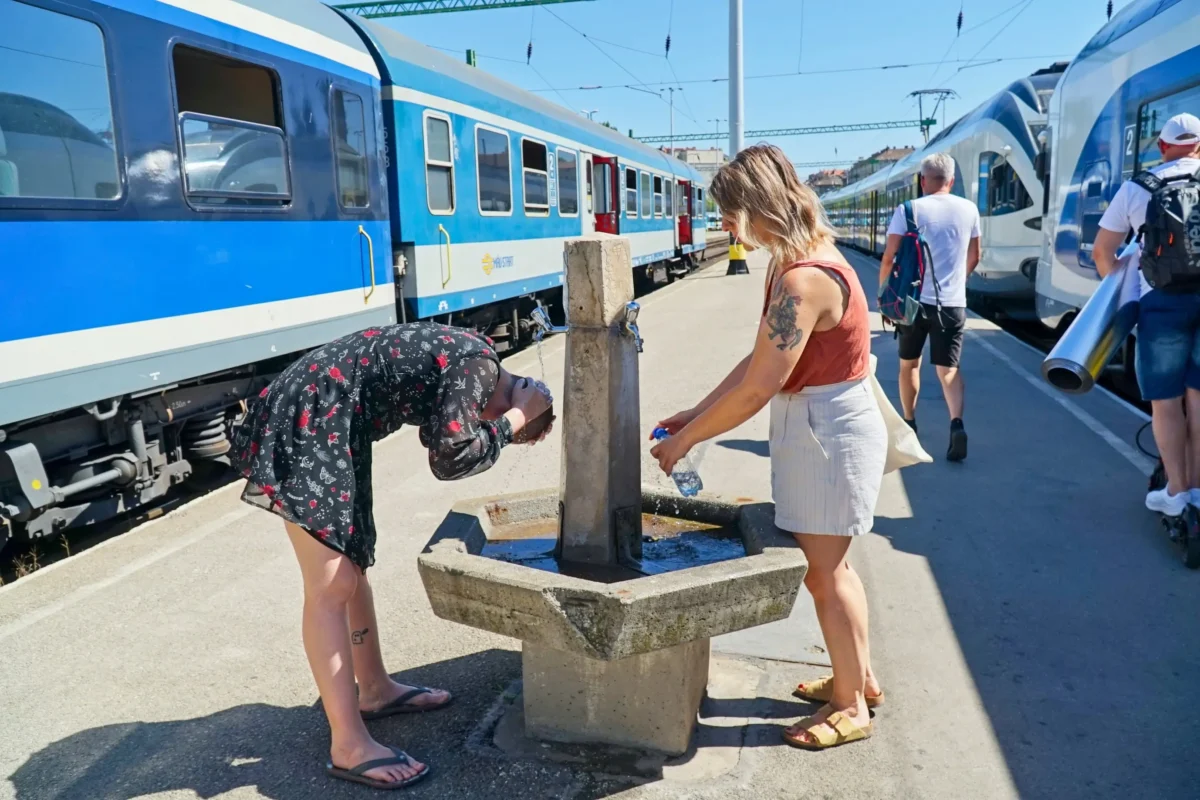 Dvě ženy se ochlazují u fontány na vlakovém nádraží.
