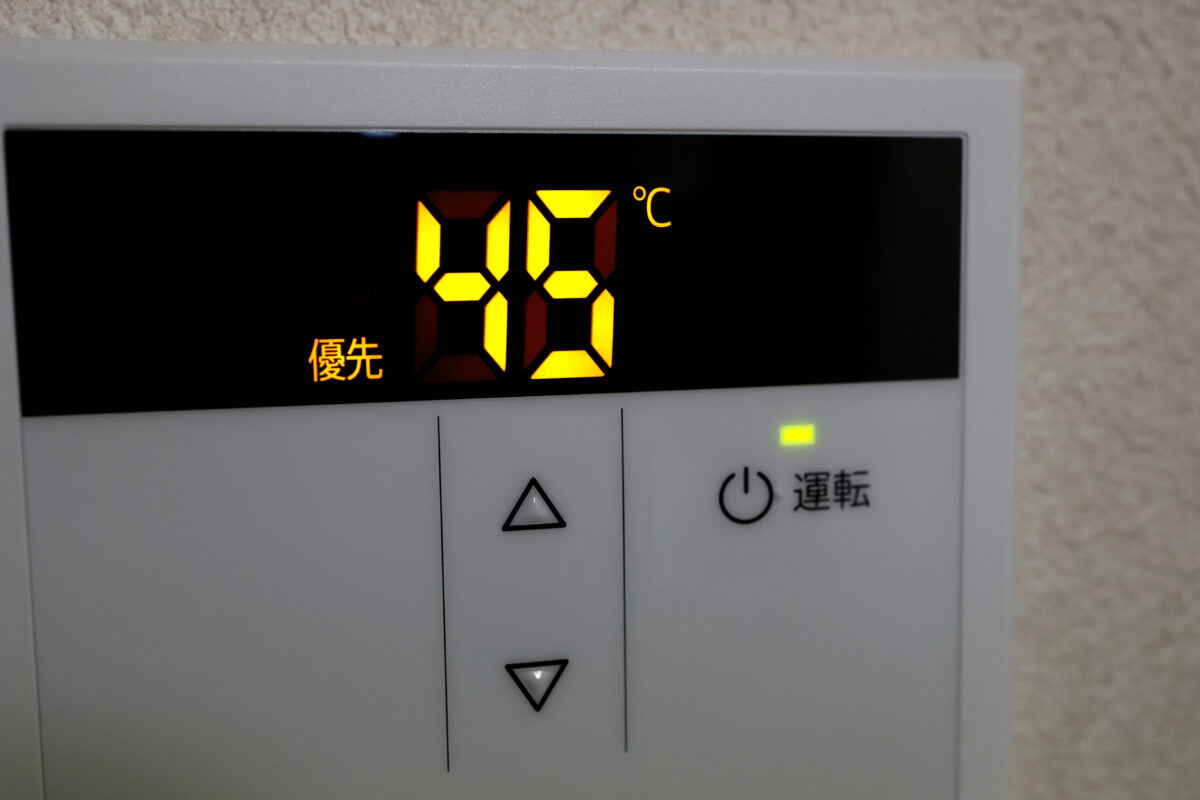 Wall-mounted control panel showing 40°C on a bright orange digital display, with the Japanese word 優先 and up/down arrow buttons beneath.