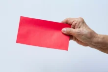 Seniorka drží v ruce červenou obálku.