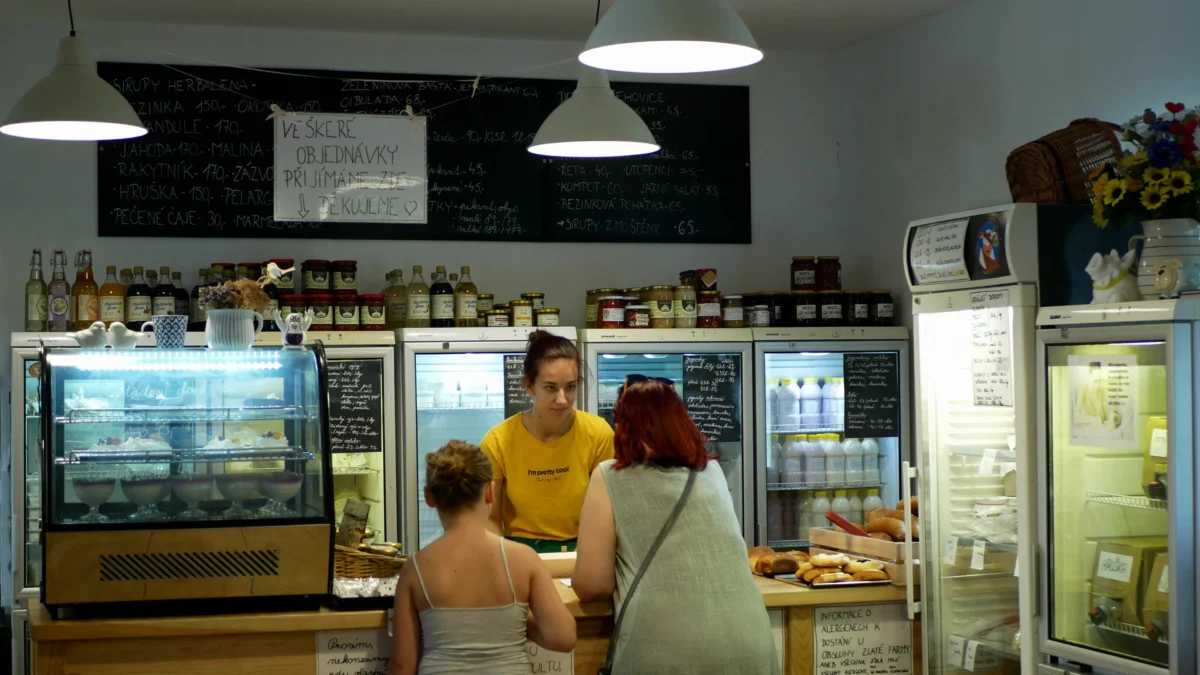 Cafe counter inside a shop with chalkboard menus, jars on shelves, and glass refrigerated displays behind the staff in yellow shirts.