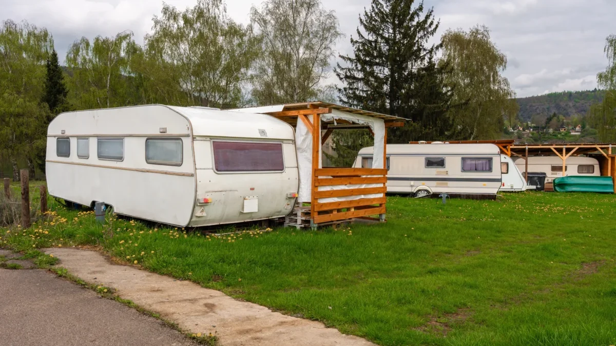 Two white caravans parked on a grassy field with a wooden shelter, under a cloudy sky and trees in the background.
