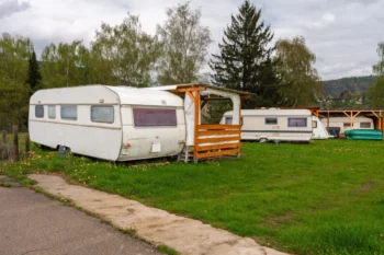 Two white caravans parked on a grassy field with a wooden shelter, under a cloudy sky and trees in the background.