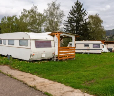 Two white caravans parked on a grassy field with a wooden shelter, under a cloudy sky and trees in the background.