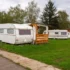 Two white caravans parked on a grassy field with a wooden shelter, under a cloudy sky and trees in the background.