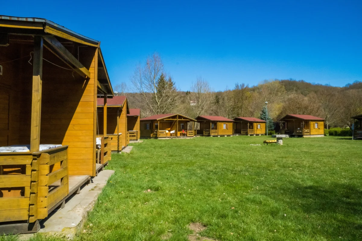 Row of wooden cabins with red roofs along a grassy field under a clear blue sky.