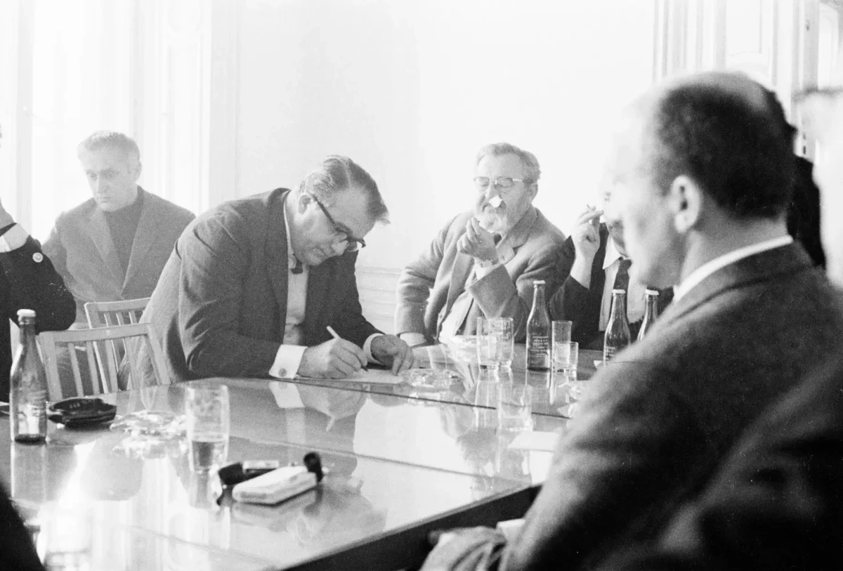 Jan Werich s dalšími lidmi sedí u stolu.