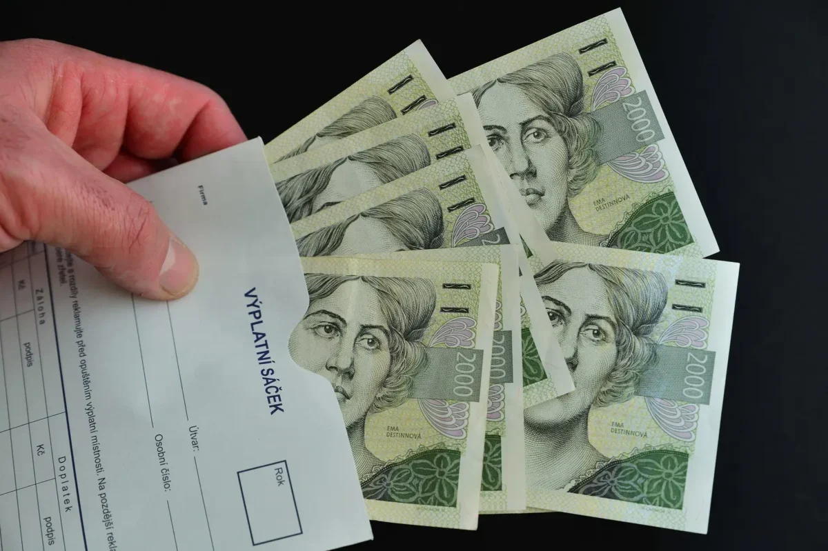 mužská ruka drží výplatní sáček s českými bankovkami