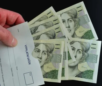 mužská ruka drží výplatní sáček s českými bankovkami