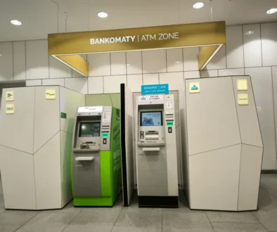 ATM machines line a modern wall inside a bank, with a sign reading 'BANKOMATY | ATM ZONE' overhead