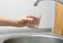 Person holds a glass under a running faucet, filling it with murky brown water.