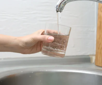 Person holds a glass under a running faucet, filling it with murky brown water.