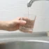 Person holds a glass under a running faucet, filling it with murky brown water.