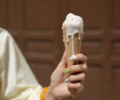Person holding a vanilla ice cream cone with melted white ice cream dripping down the cone, bokeh background.