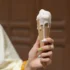 Person holding a vanilla ice cream cone with melted white ice cream dripping down the cone, bokeh background.